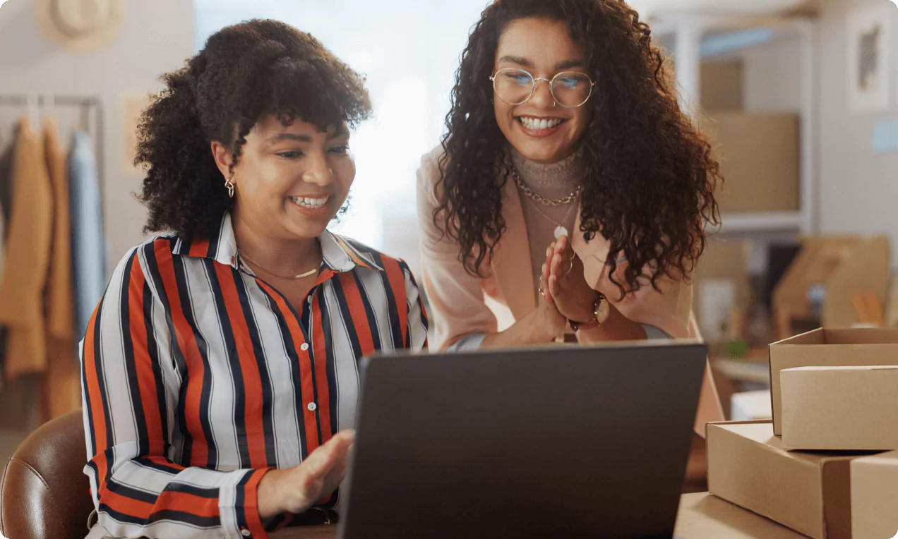 Two smiling women using a laptop in a fashion store.